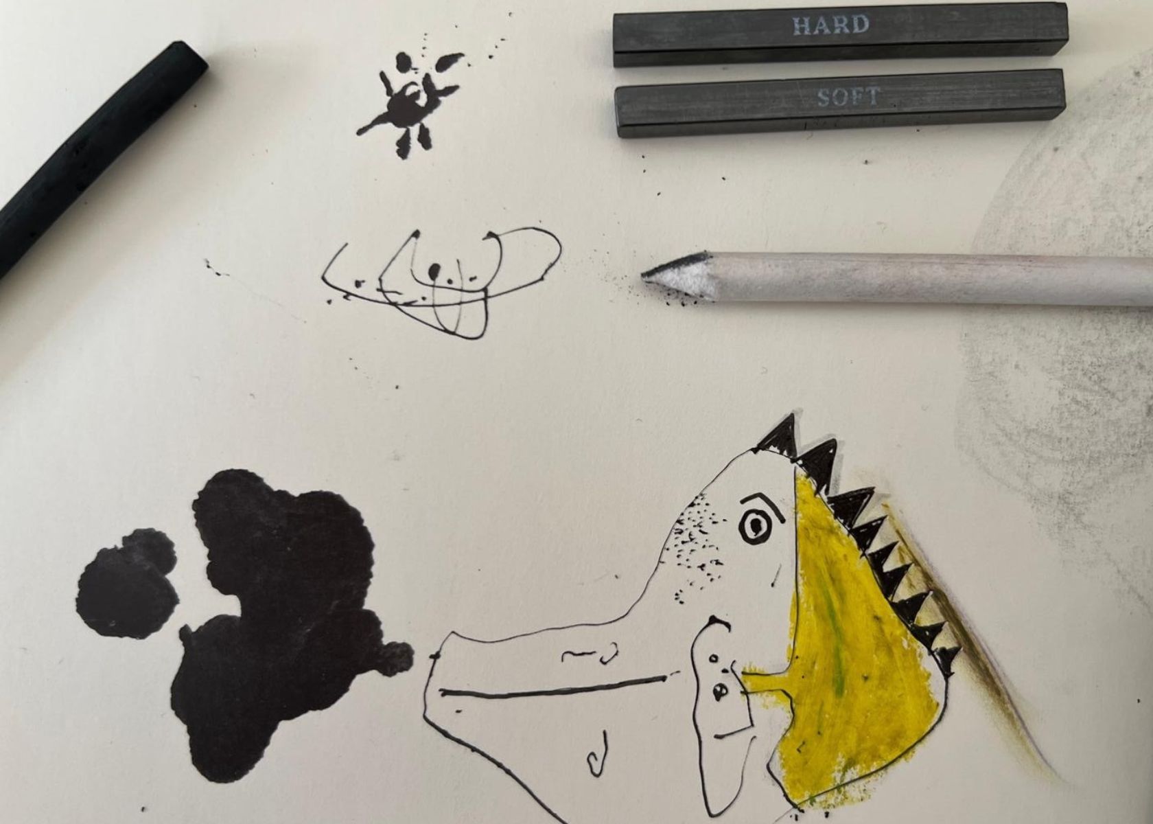 Studio desk with charcoal, ink blot and a small creature sketch